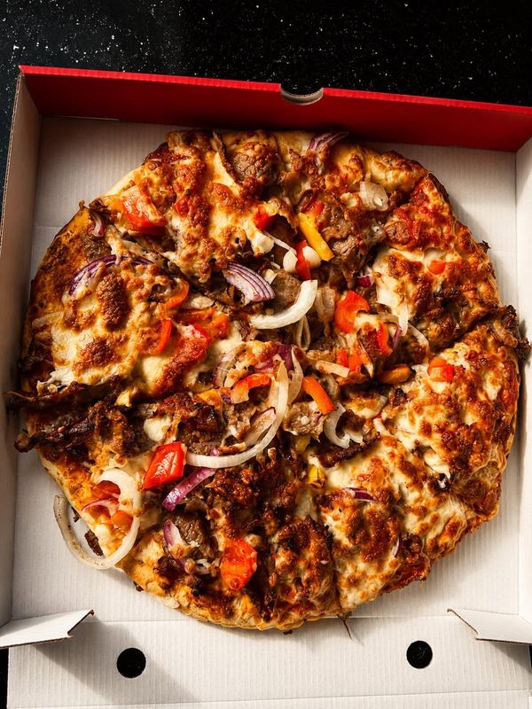Freshly baked pizza loaded with doner meat, peppers and onions in an open pizza box